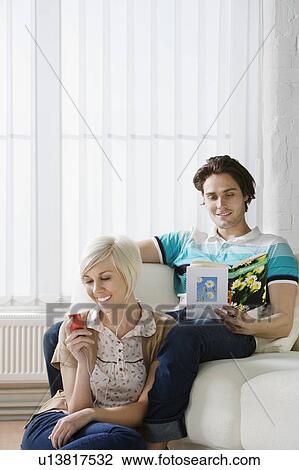 Stock Image - Young woman listening mp3 player next to man reading book on sofa. Fotosearch