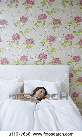 Stock Photograph - Young woman lying in bed, smiling. Fotosearch