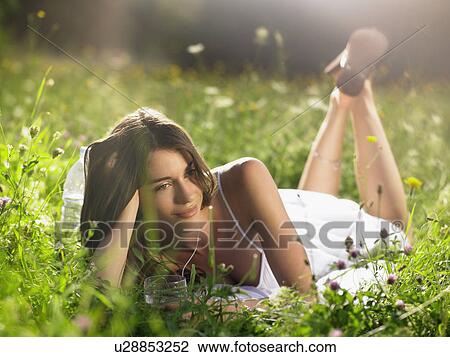 Stock Image - Young woman lying in meadow, leaning on elbow. Fotosearch