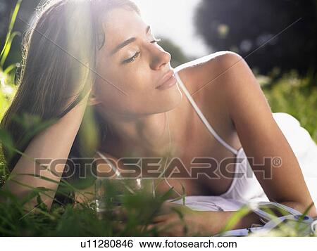 Stock Photograph - Young woman lying in meadow, leaning on elbow, with drinking glass. Fotosearch