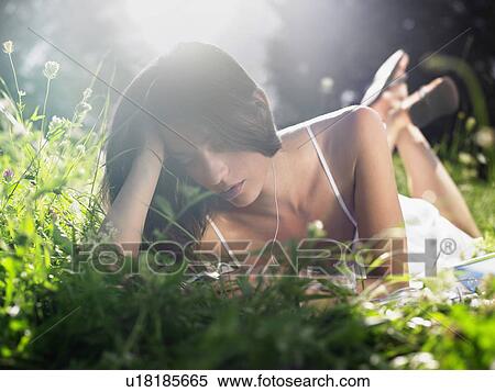 Young woman lying in meadow listening to mp3 player View Large Photo Image Stock Photography - Young woman lying in meadow listening to mp3 player. Fotosearch