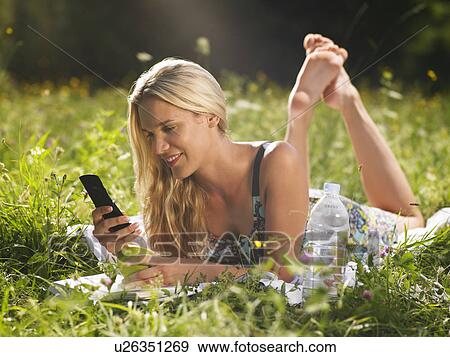 Stock Photo - Young woman lying in meadow using mobile phone. Fotosearch