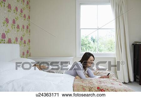 Young woman lying on bed holding mobile phone, smiling View Large Photo Image Stock Image - Young woman lying on bed holding mobile phone, smiling. Fotosearch