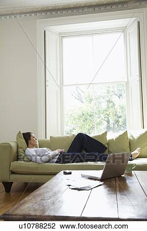 Stock Image - Young woman lying on sofa. Fotosearch