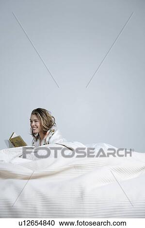 Young woman reading book in bed, smiling View Large Photo Image Stock Image - Young woman reading book in bed, smiling. Fotosearch