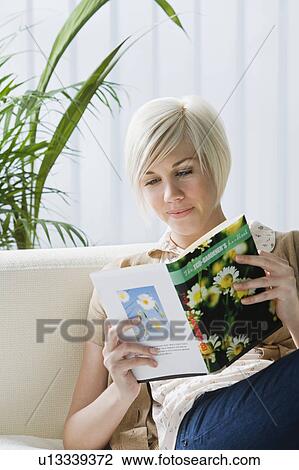 Stock Image - Young woman reading book on sofa. Fotosearch