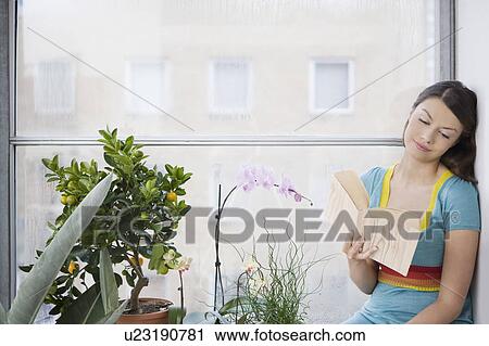 Young woman reading book, sitting on window sill View Large Photo Image Stock Image - Young woman reading book, sitting on window sill. Fotosearch