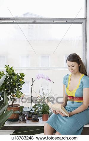 Stock Photo - Young woman reading book, sitting on window sill . Fotosearch