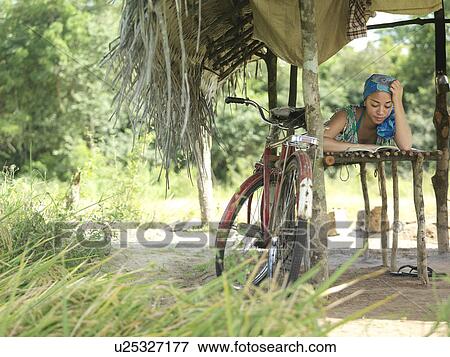 Stock Photo - Young woman reading in hut, bicycle leaning on pale. Fotosearch