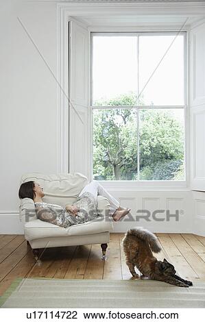 Young woman relaxing on armchair with cat stretching on floor View Large Photo Image Stock Image - Young woman relaxing on armchair with cat stretching on floor. Fotosearch
