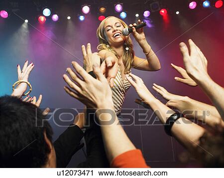 Stock Image - Young Woman Singing in Concert reaching out to fans, low angle view. Fotosearch
