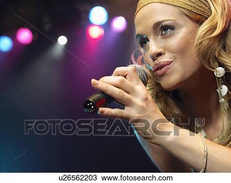 Stock Image - Young Woman Singing on stage in Concert, close up, low angle view. Fotosearch