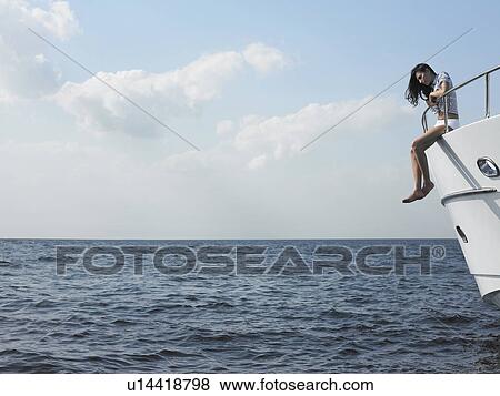 Young woman sitting at edge of yacht with legs dangling overboard, side view View Large Photo Image Stock Photo - Young woman sitting at edge of yacht with legs dangling overboard, side view. Fotosearch