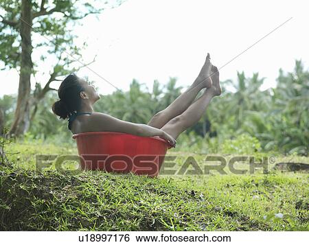 Stock Photograph - Young woman sitting in bowl outdoors, side view. Fotosearch