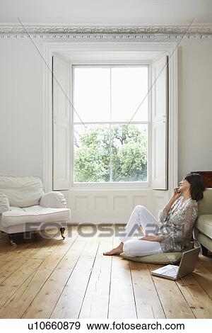 Stock Photo - Young woman sitting on floor, talking on mobile. Fotosearch
