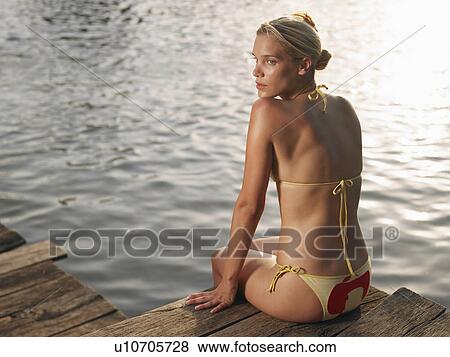 Young woman sitting on jetty, looking over shoulder, back view View Large Photo Image Stock Photo - Young woman sitting on jetty, looking over shoulder, back view. Fotosearch