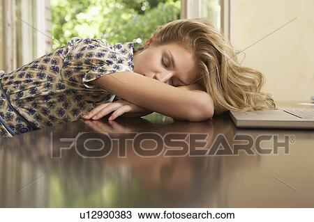 Stock Image - Young woman sleeping in front of laptop in living room. Fotosearch