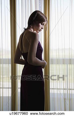 Stock Image - Young woman standing by window, back view. Fotosearch