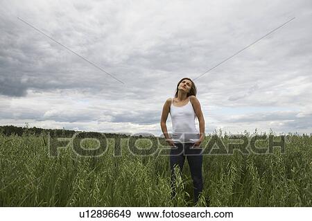 Young woman standing on field View Large Photo Image Stock Photo - Young woman standing on field. Fotosearch