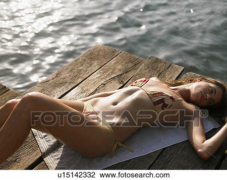 Stock Image - Young woman sunbathing on jetty, elevated view. Fotosearch