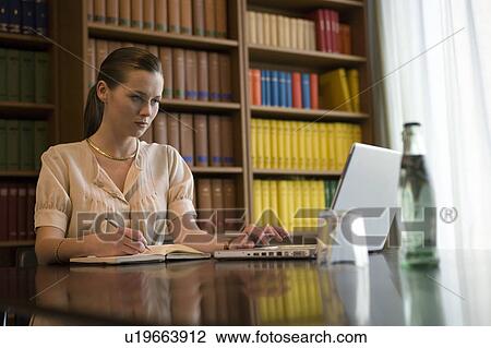 Young woman using laptop at desk in library View Large Photo Image Stock Image - Young woman using laptop at desk in library. Fotosearch
