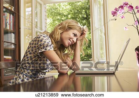 Stock Photo - Young woman using laptop in living room. Fotosearch