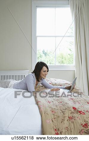 Young woman using laptop lying on bed View Large Photo Image Stock Photo - Young woman using laptop lying on bed. Fotosearch