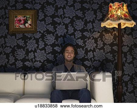 Stock Photo - Young woman using laptop sitting on sofa. Fotosearch