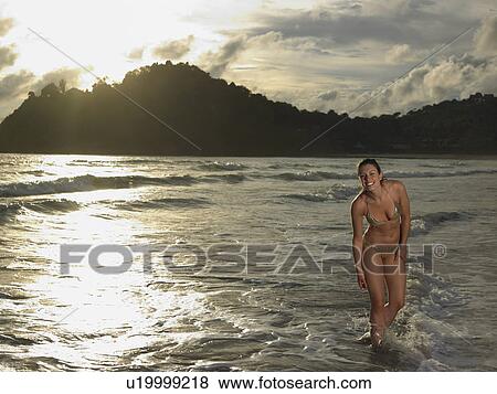 Stock Photo - Young Woman Wading in Ocean at Sunset. Fotosearch