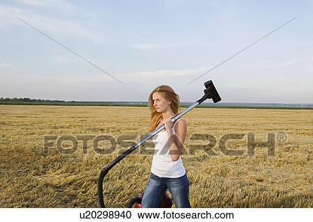 Stock Image - Young Woman Walking in a Field with a Vacuum Cleaner. Fotosearch