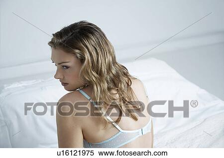 Stock Photography - Young woman wearing bra sitting on bed, elevated view. Fotosearch