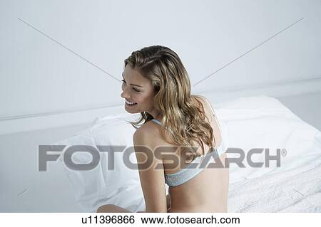 Stock Photograph - Young woman wearing bra, smiling on bed, elevated view. Fotosearch