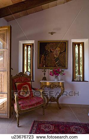 Stock Image - Antique chair and marble-topped gilt console table in small Mediterranean hall. Fotosearch