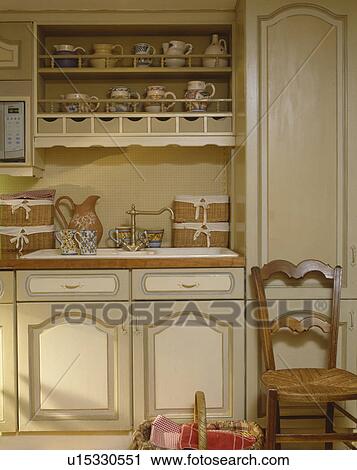 Antique chair in front of built in sink below storage shelves in cream painted kitchen View Large Photo Image Stock Image - Antique chair in front of built in sink below storage shelves in cream painted kitchen . Fotosearch