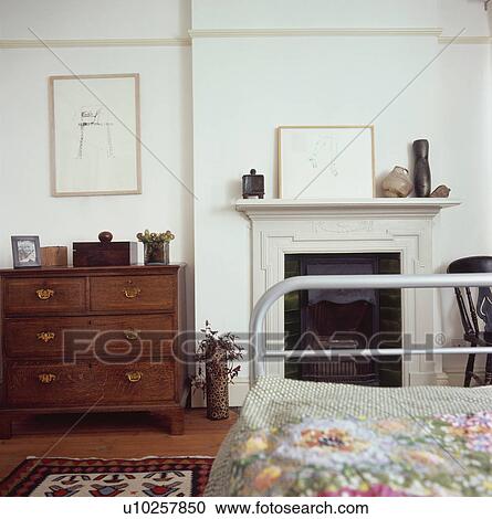 Antique Chest Of Drawers Beside Fireplace In Small White Bedroom