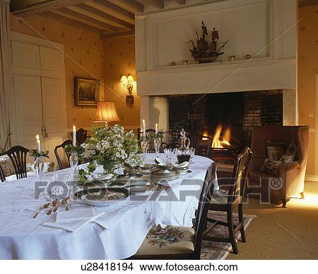 Picture - Antique china and white linen cloth on long table in French country dining room with large stone fireplace. Fotosearch