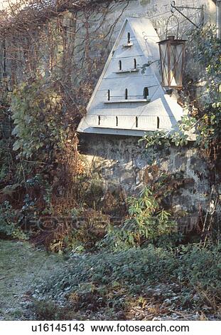 Stock Image - Antique dovecote and lantern on old stone wall in garden. Fotosearch