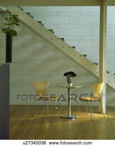Stock Photograph - Arne Jacobsen Ant chairs in small steel table below staircase in modern hall dining room. Fotosearch