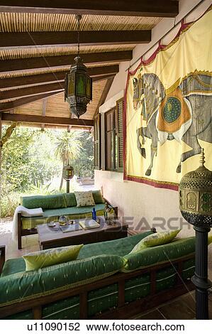 Stock Image - Bamboo ceiling and metal lantern on veranda with Rajasthan wall-hanging and green sofas. Fotosearch