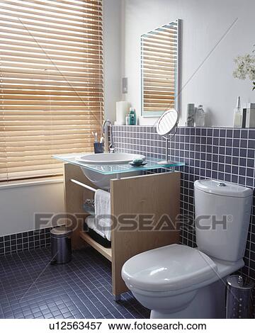 Stock Photo - Basin in wooden vanity unit beside window with slatted blind in modern bathroom. Fotosearch
