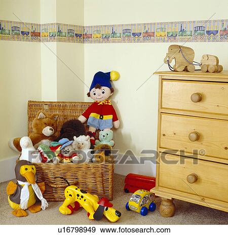 Basket of colourful soft toys beside pine chest of drawers in child's bedroom with wallpaper frieze View Large Photo Image Stock Photo - Basket of colourful soft toys beside pine chest of drawers in child's bedroom with wallpaper frieze. Fotosearch