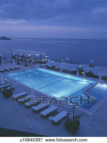 Beachside cafe and loungers beside swimming pool underlit at night View Large Photo Image Stock Photo - Beachside cafe and loungers beside swimming pool underlit at night . Fotosearch