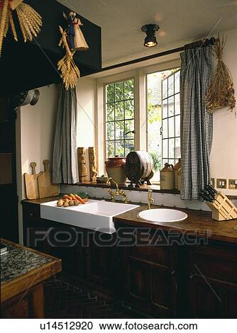Belfast sink and circular white sink in worktop below window with checked drapes in small country kitchen View Large Photo Image Stock Image - Belfast sink and circular white sink in worktop below window with checked drapes in small country kitchen. Fotosearch
