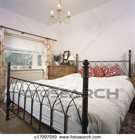 Black cast-iron bed with red cushions and white bedlinen in small country bedroom View Large Photo Image Stock Photo - Black cast-iron bed with red cushions and white bedlinen in small country bedroom. Fotosearch
