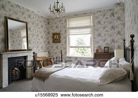 Black Iron Bed With White Bedlinen In Traditional Bedroom With Victorian Patterned Wallpaper And Marble Fireplace Stock Photography