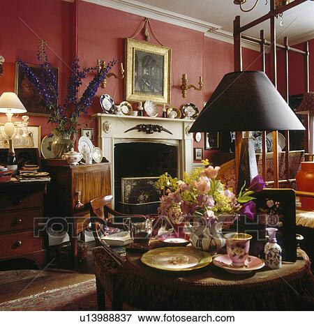 Stock Photo - Black lamp and antique china with small flower arrangement on table in red townhouse living room&#10; &#10;. Fotosearch