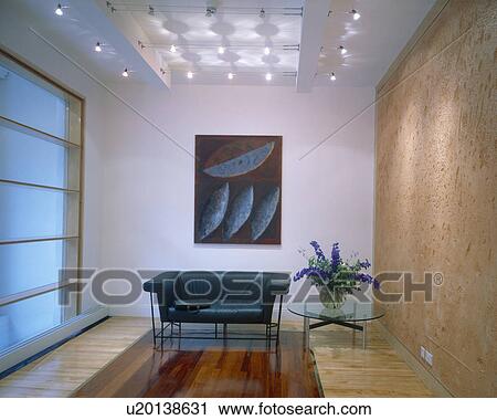 Stock Image - Black leather sofa below ceiling lights in office reception area with textured stone wall. Fotosearch