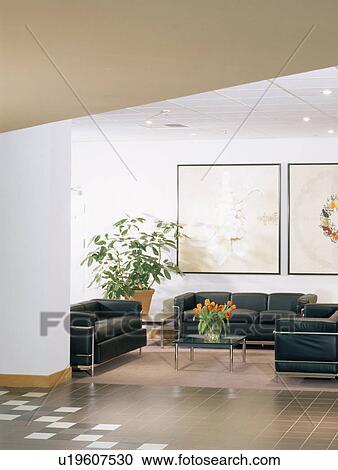 Stock Image - Black leather+chrome sofas in modern living room with grey floor tiles. Fotosearch