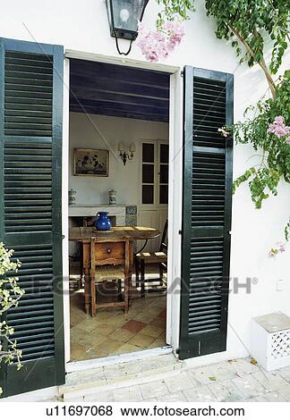 Stock Photo - Black louvre shutters on French windows with view of dining room in Mallorcan house. Fotosearch