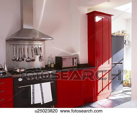 Stock Image - Black range oven in modern white kitchen with red fitted units. Fotosearch